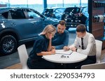 Small photo of Happy caucasian couple signs a contract for the purchase of a car salon.