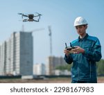 Small photo of A man in a helmet and overalls controls a drone at a construction site. The builder carries out technical oversight.