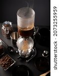 Small photo of Vacuum coffee maker also known as vac pot, siphon or syphon coffee maker and toasted coffee beans on rustic black stone table.