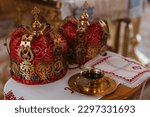 Small photo of Closeup view to two red wedding crowns on embroidered towel and bowl with sanctified water during a wedding ceremony in Orthodox Ukrainian church.