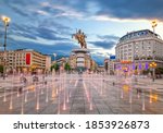 Small photo of Skopje, North Macedonia - 01.08.2020: Square Macedonia in Skopje at sunset with dancing illuminated fountains and statue of Alexander the Great (warrior on horse) at background