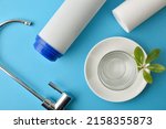 Small photo of Set of domestic reverse osmosis filters and glass with purified water on a plate with green leaves on a blue table. Top view. Horizontal composition.