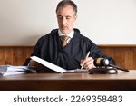Small photo of Judge sitting in an armchair reviewing the summary of a case on a wooden table. Front view