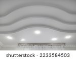 suspended ceiling with halogen spots lamps and drywall construction  with intricate crown molding in empty room in apartment or house. Stretch ceiling white and complex shape.