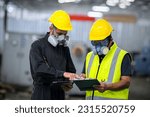 Small photo of Two officers wearing gas masks, holding tablet and book, inspect the chemical spill site in an industrial warehouse to assess the damage, wearing gas masks, inspecting and evaluating toxicity of leak.
