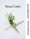 Small photo of Blessed Imbolc greeting card. ireland amulet from straw and snowdrops flowers in snow natural background. Brigid's cross, symbol of Imbolc sabbat. spring-winter festive Wiccan tradition ritual