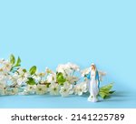 Miniature statue of the Virgin Mary and white spring flowers on blue background. symbol of Christianity religion. faith in God concept. Feast of Annunciation to the Blessed Virgin Mary