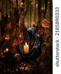 Small photo of Magician, black cloaked figure with burning candle in dark forest, mystery natural background. esoteric spiritual ritual for Samhain sabbat, Halloween holiday. Grim Reaper, witchcraft ritual