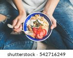 Eating healthy breakfast bowl. Yogurt, granola, seeds, fresh and dry fruits and honey in blue ceramic bowl in woman' s hands. Clean eating, dieting, detox, vegetarian food concept