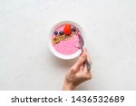 Woman's hand holding spoon in the Smoothie bowl with fresh berries, golden and brown flax seeds. Healthy breakfast, fitness, diet concept. White stone background. Top view. Copy space.