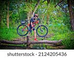 Small photo of woman cyclist in action of carry owns mountain bicycle crossing the small clack of ditch canal in the jungle forest, extreme riding sport trail in the route of competitive area