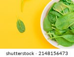 Fresh Baby Spinach Leaves in White Bowl on Yellow Background - Top View. Vegan and Vegetarian Culture. Raw Food, Green Leaves. Healthy Diet