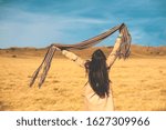 Small photo of Happy woman is jumping with her scarf up, enjoying life in a golden grass field on a wonderful sunny day.