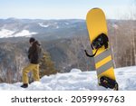Small photo of The snowboard stands in the mountains while the snowboarder admires the views from the top of the mountains. Active winter recreation