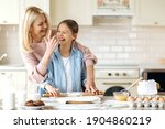 Small photo of Cheerful mom or grandma and her pretty little daughter or granddaughter spend time together at the kitchen. They cook together a pie, indulge in flour, laugh and have fun