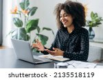 Successful positive young adult woman african woman freelancer, manager, CEO, sitting in office at laptop, talking on video call with client or employees, discussing business strategy, gesturing,smile