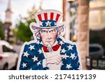 Small photo of Uncle Sam holding a blank white sign and staring directly at you or viewer or camera in star spangled outfit with red white and blue American USA outfit with red bow tie star decorated suit top hat.