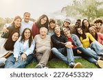 Happy multigenerational people having fun sitting on grass in a public park - People diversity concept