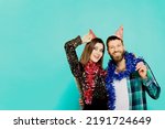 Small photo of A man and a woman 20-25s in party hats and New Year's tinsel hugging, laughing and looking at the camera on a mint isolated background. Party banner with copy space