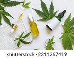 Cosmetic dropper bottles with blank label near green cannabis sativa leaves on a marble table top view. Mockup, Copy space. Organic skincare beauty products. Eco friendly CBD oil