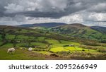 The rolling agricultural hills of mid Wales. The landscape is Talybont, on a cloudy day, with a shaft of sunlight spotlighting a small section of the countryside