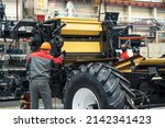 Worker assembles agricultural vehicle combine harvester in industrial factory workshop