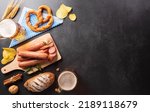 Small photo of Oktoberfest festival decoration symbols made from Pretzel loaf, beer, sausage, potato chips and Bavarian white and blue fabric on dark stone background.