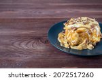 Small photo of Sweet delicious dessert a cinnamon bun sprinkled with pecans and poured with caramel topping on a black plate and a turd background. Copy space