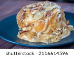 Small photo of Sweet delicious dessert a cinnamon bun sprinkled with pecans and poured with caramel topping on a black plate and a turd background.