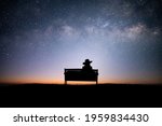 Silhouette of young woman sitting on old wooden chair looking at the night sky and looking at the beauty of the stars and the Milky Way alone on top of the mountain.