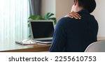 Small photo of Panorama of young businessman sitting on the desk in the living room at home. He used hands to press down on the shoulder and neck. He is suffering from neck pain from sitting for a long time.