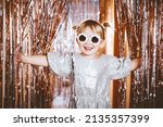 Small photo of Happy little stylish girl in shiny dress having fun. Festive background with foil curtain decorations for kids birthday or fancy dress party, disco music or New Year. Celebration and Holiday concept.