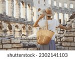 Beautiful tourist woman in Roman Amphitheater Arena like Coliseum - famous travel destination in Pula, Croatia. Female traveler visiting the sights. Vacation in Europe at summertime.