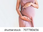 Pregnant woman in dress holds...