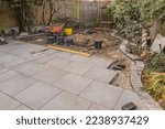 Garden paving under construction, with grey porcelain patio tiles and curved charcoal edge bricks.