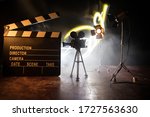 Movie concept. Miniature movie set on dark toned background with fog and empty space. Silhouette of vintage camera on tripod and clapboard. Selective focus
