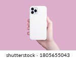 Female hand holding white iPhone 11 Pro in soft silicone white cover back view . Phone case mock up isolated on pink background
