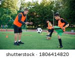 Small photo of Young soccer coach instructs teen players. A young professional coach trains the ball kicks with young football players.