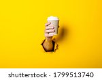 Man's hand holds a paper cup with coffee closed by a bump on a bright yellow background