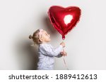 Little girl holding a heart air balloon and looks at it on a light background. Concept for Valentine's Day, birthday. Banner.