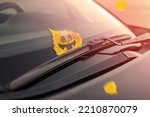 Cheerful yellow leaf with emotion, on the windshield of the car under the brush. Concept of warm autumn or Halloween holiday. Toned background