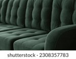 Quilted vintage sofa background in emerald velour fabric. Stitched elegant vintage upholstered furniture with a blurred background. Lateral part of a sofa with the stitched elbow.