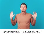 Small photo of I give up! Attractive unshaven stylish man shows palms, demonstrates his innocence, surrenders, isolated over blue background. Handsome young male raises hands, looks puzzled, feels guiltless