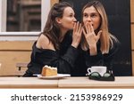 Small photo of Gossiping. Two beautiful young women gossiping telling something on ear while sitting in the cafe. Communication and friendship concept. Young woman telling her friend some secrets.