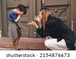Small photo of Mother scolds her son on the street. A child cries, a woman shakes her finger because of the boy bad behavior, while walking to home. Rule of conduct. Woman sitting, boy cover his face and cry.
