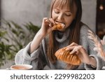 Small photo of Young blonde woman with bang eating croissants at a cafe. Girl bite piece of croissant look joyful at restaurant. Cheat meal day concept. Woman is preparing with appetite to eat croissant.