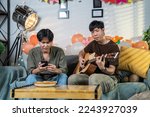 Small photo of Two Asian friends play guitar while the other holds a smartphone to sing along to the lyrics on their cell phone during a party in house