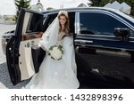 Beautiful Bride with Flower Bouquet in Limousine. Pretty Young Woman Wearing White Wedding Dress and Tiara with Veil. Girl Holding in Hand Roses Bunch and Sitting in Black Limo Car. Outside Photo