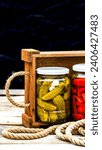 Small photo of Wooden crate with glass jars with pickled red bell peppers and pickled cucumbers (pickles) isolated. Jars with variety of pickled vegetables. Preserved food concept in a rustic composition.