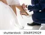 Small photo of polite man helps a woman to put on her shoes. The groom takes care of his bride and on the wedding day neatly buttons up women's high-heeled shoes. Female shoes and male hands close up